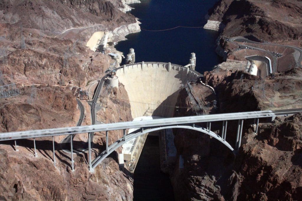 An aerial view of Hoover Dam, featuring the extensive bridge in front of the dam, and water on both sides.