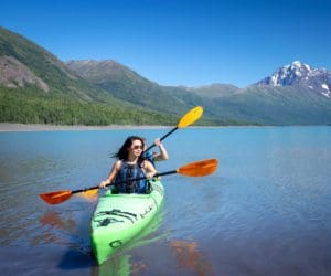 A mother and son tandem kayak along Eklutna, with mountains in the distance, near Anchorage.
