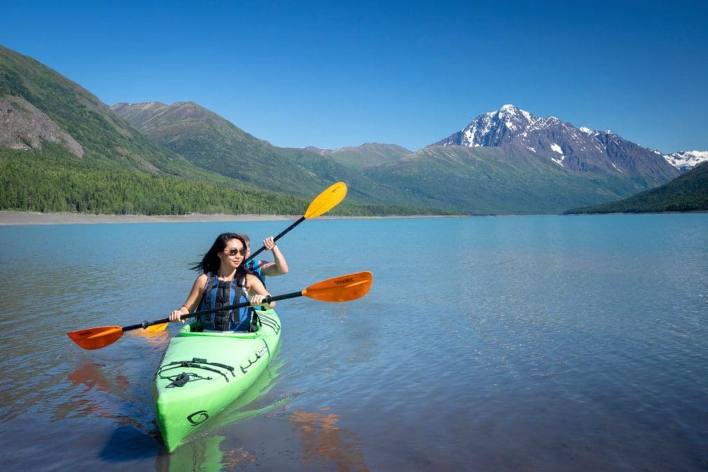 A mother and son tandem kayak along Eklutna, with mountains in the distance, near Anchorage, one of the best cool-weather destinations in the United States for families.