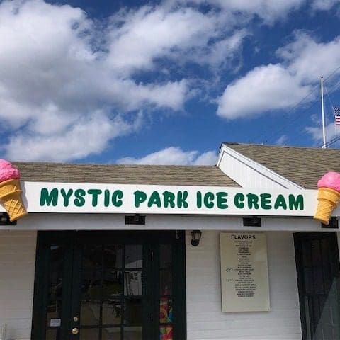 A close up of the exterior sign for Mystic Park Ice Cream, with clouds and blue skies overhead.