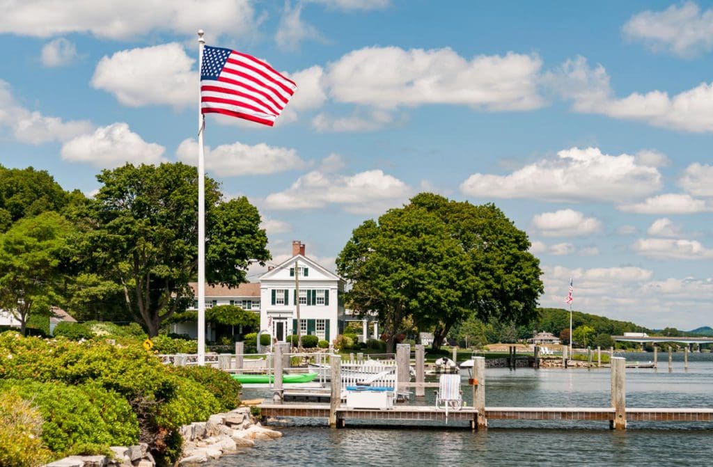 A large American flag flies overhead near the seaport at Mystic on a sunny day, one of the best Fourth of July destinations for a family trip.