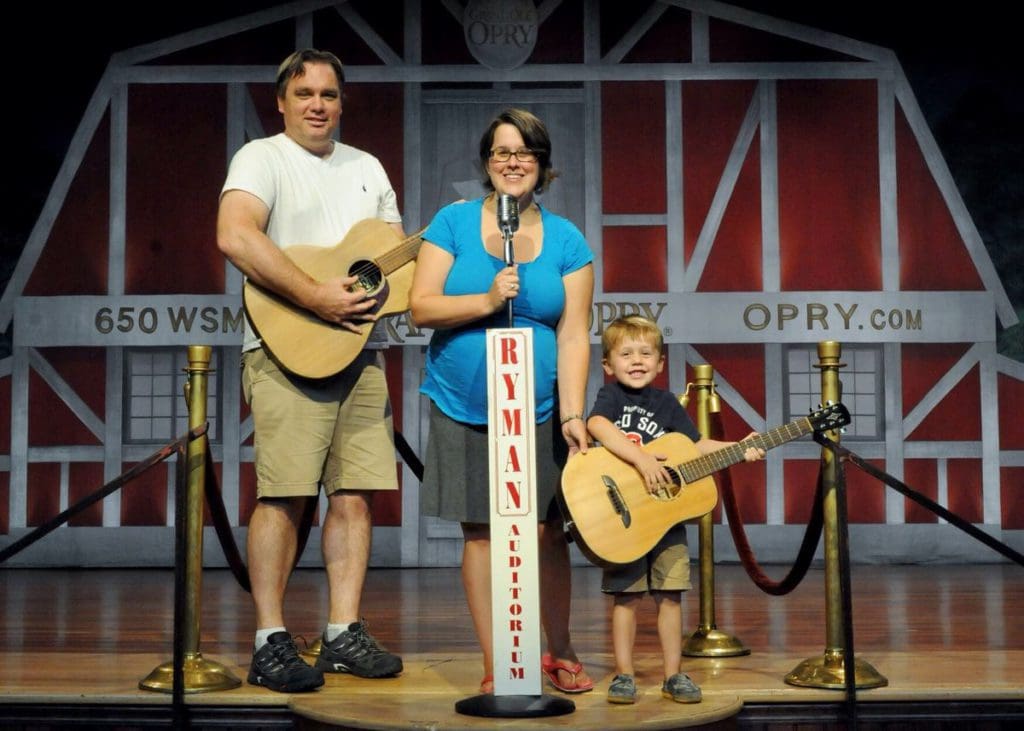 A dad and son play guitars on stage at Ryman Auditorium, while mom sings between them.
