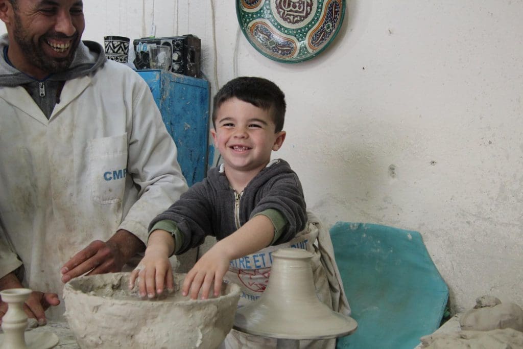 A young boy puts his hands in wet clay, as he and a guide make a bowl as part of a tour in Morocco.