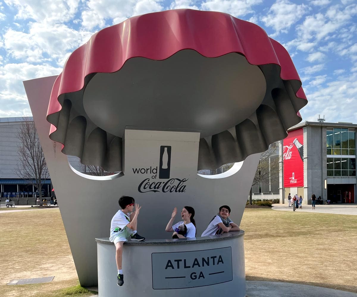 Three kids sit amongst the Coca-Cola statue outside Coca-Cola World in Atlanta, one of the best US cities for a Memorial Day Weekend with kids.