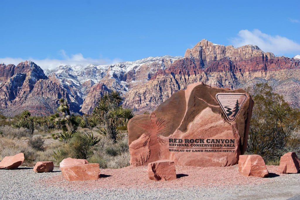 The sign for Red Rock Canyon National Conservation Area, with a scenic view of the red rocks in the distance.