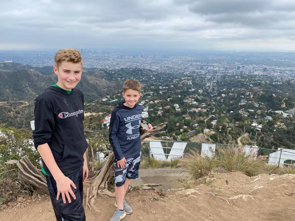 Two older boys stand on a hill above the Hollywood Sign with the LA cityscape in the distance.