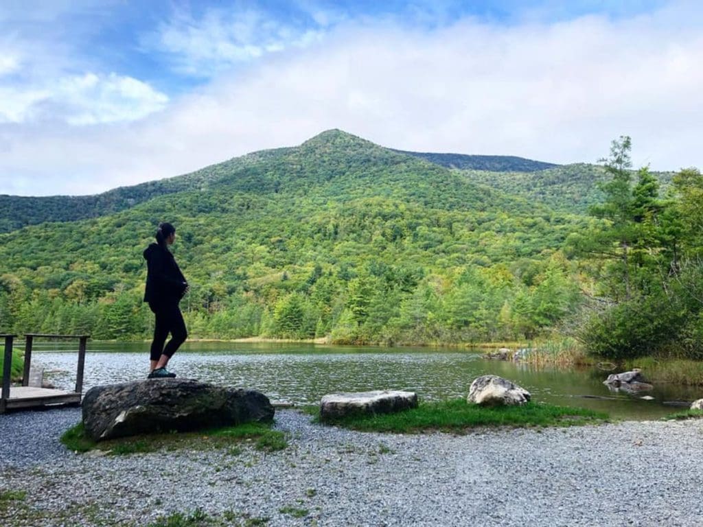 A teenagers stands on a large rock along the lake shore in Manchester, Vermont, one of the best cool-weather destinations in the United States for families.