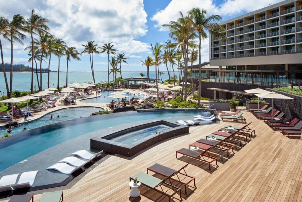 A pool deck at Turtle Bay, facing the pool, with the ocean in the distance, one of the best hotels in Hawaii for a family vacation.