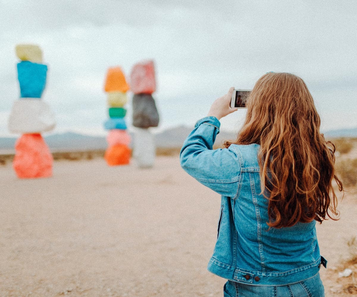 A woman takes a picture of Seven Magic Mountains near Las Vegas, one of the best US cities for a Memorial Day Weekend with kids.