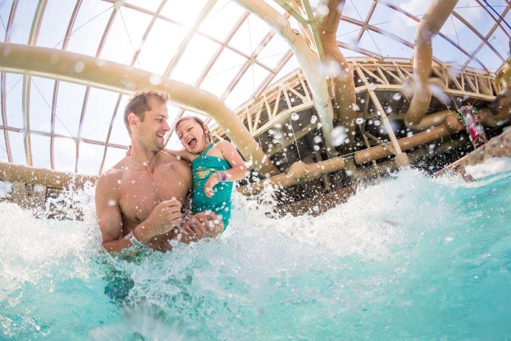 A dad holds and spins his young daughter, while standing hip-deep in a pool inside the indoor water park at Wilderness Resort.