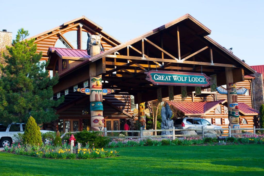 The outdoor entrance to Great Wolf Lodge in the Wisconsin Dells, featuring totem pole columns and lush green grass.
