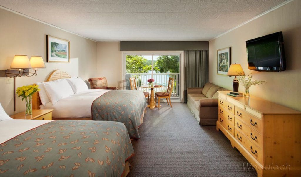 Inside a guest room at Woodloch Resort, featuring two double beds, a tv, small table and chairs, and view out onto the lovely resort grounds.