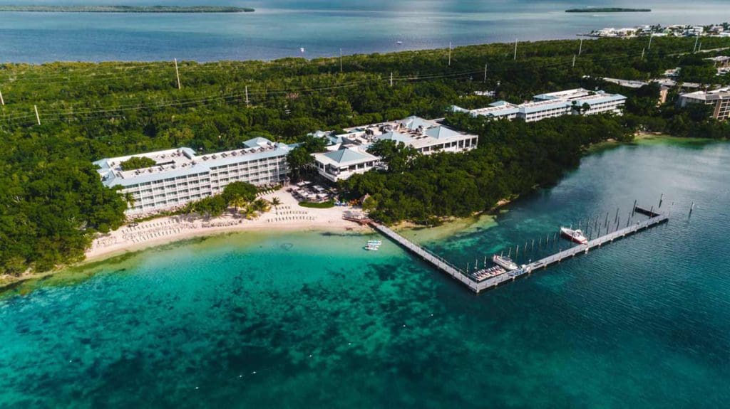An aerial view of Baker's Cay Resort Key Largo, Curio Collection By Hilton, nestled along the shore of the ocean near Key Largo, and surrounded by lush greens.