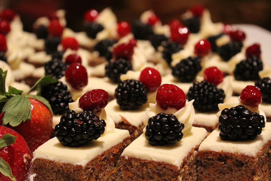 A tray filled with small luxury cake slices, featuring frosting with either a blackberry or a strawberry on the,.
