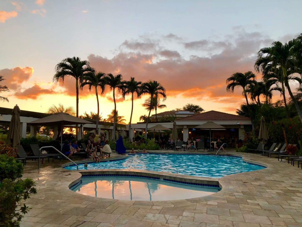 The pool at Maui Coast Hotel, surrounded by resort buildings, at sunset at one of the best hotels in Hawaii for a family vacation.