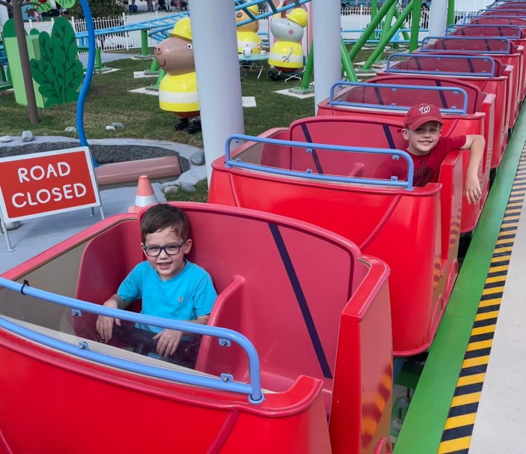 Two kids sitting in separate roller coaster cars at Peppe Pig Theme Park in Florida.