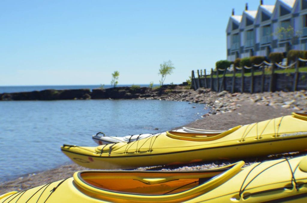 Two yellow sea kayaks sit on the shore of Lake Superior with Bluefin Bay in the distance.