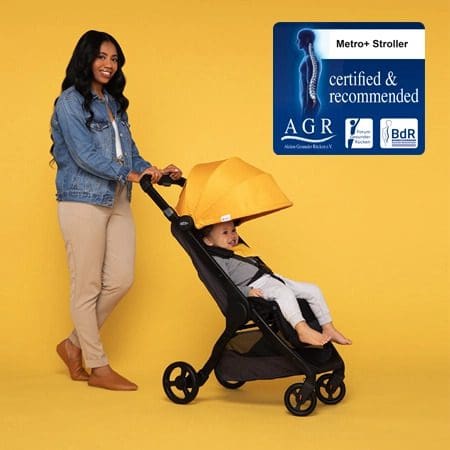 A mom pushes her young child in a yellow Ergo Baby Metro Plus.