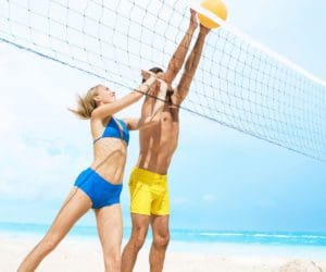 A man and woman, both in swimsuits, meet at a volleyball net on the beach to push the ball over the net at Finest Playa Mujeres in Cancun.