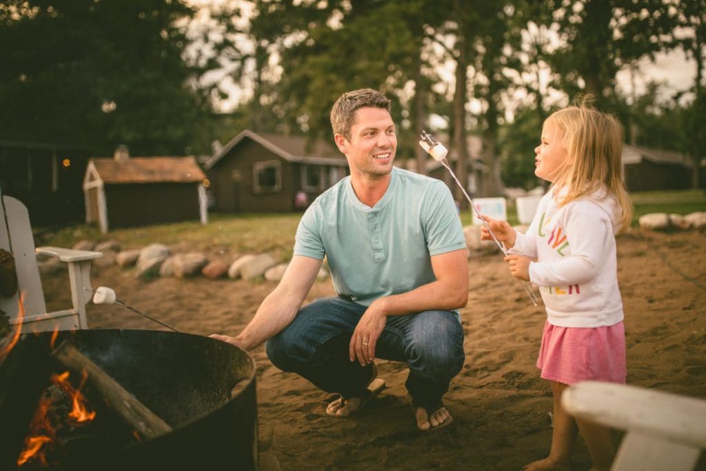 A dad and his young daughter roast marshmallows together on a beautiful summer evening.