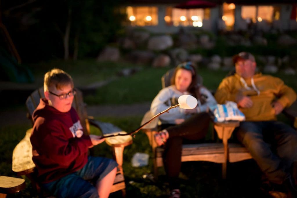 A family of three hangs out around a campfire at Gunflint Lodge & Outfitters, roasting marshmallows.