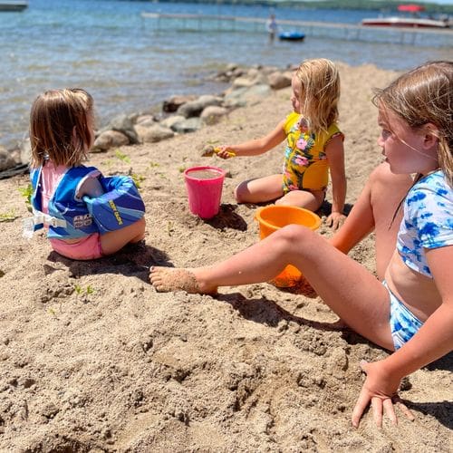 Three kids sit and play on the beach with several beach toys at Kavanaugh’s Sylvan Lake Resort.