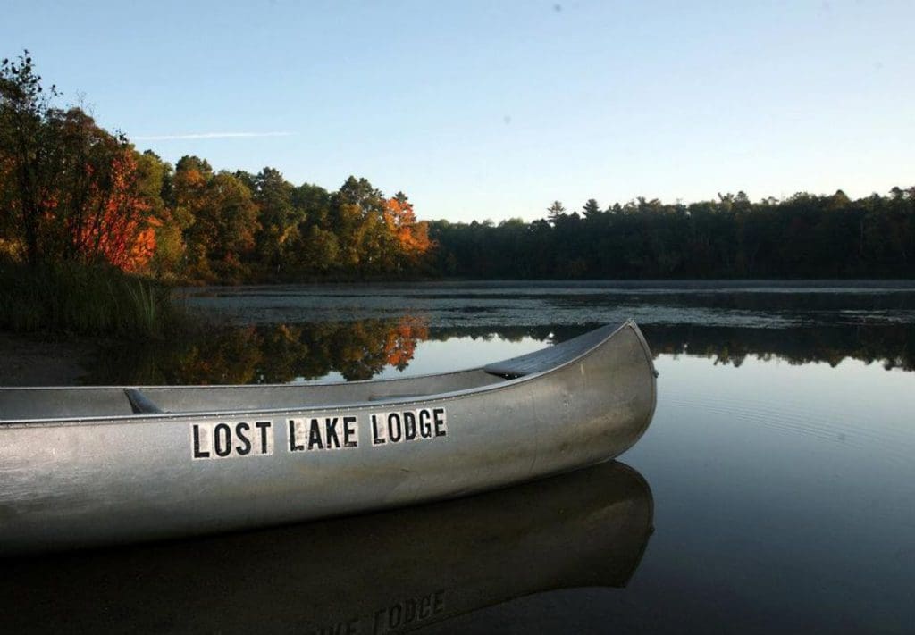 A canoe with sticker letters on the side reading "Lost Lake Lodge" sits on a still lake.