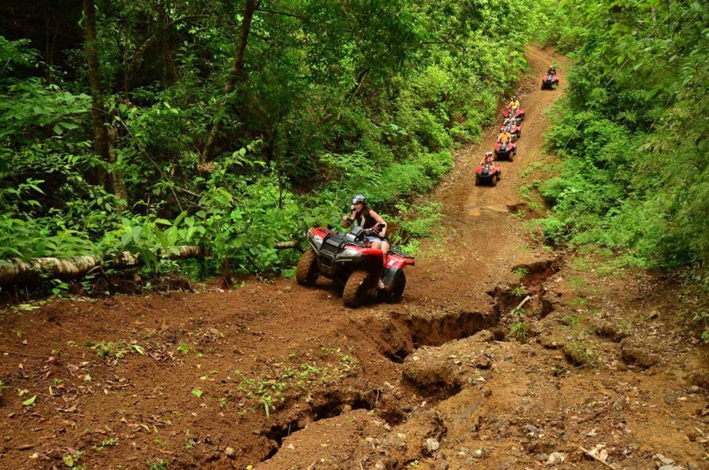 Several people riding ATVs ride up a huge, muddy trail in Costa Rica, with lush foliage flanking the trail on both sides.