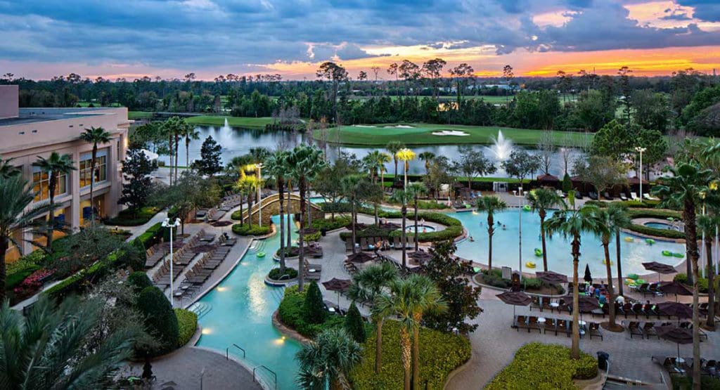 An aerial view of the outdoor pools, surrounded by lush greenery and palms trees, at Signia by Hilton Orlando Bonnet Creek.