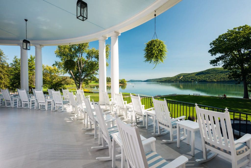 Classic white rocking chairs line the veranda, with a view of the water, of The Otesaga Resort Hotel. 
