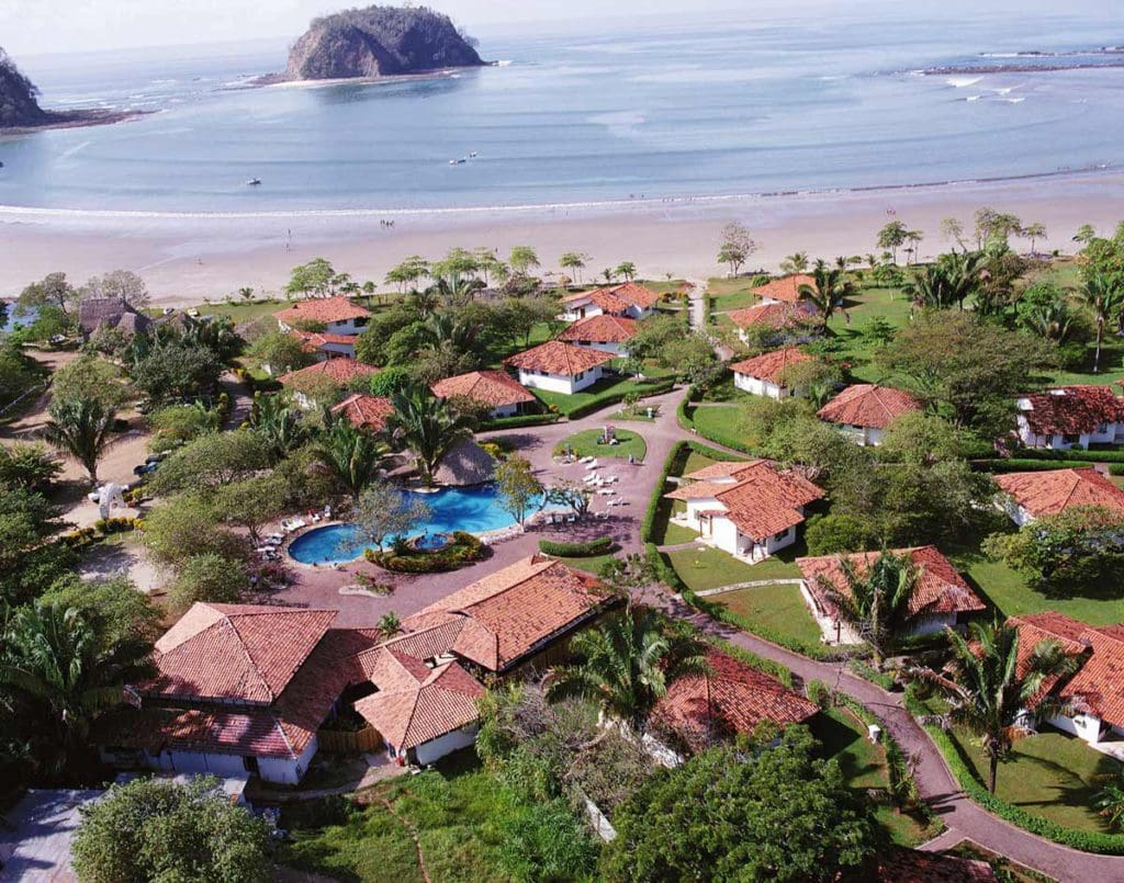 An aerial view of Hotel Villas Playa Samara, featuring red-roofed villas, intimate pools, lush foliage, and beachfront access.