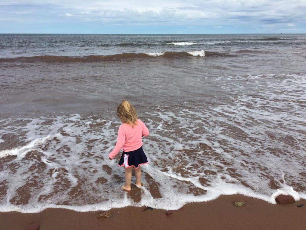 A young girl sticks her toes in the water on a beach in Prince Edward Island, one of the best vacation destinations for families In Canada.