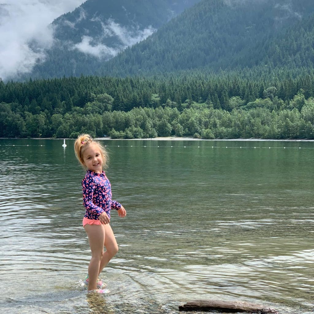 A young girl wearing a swimming suit stands on the shores of the lake within Golden Ears Provincial Park in British Colombia,