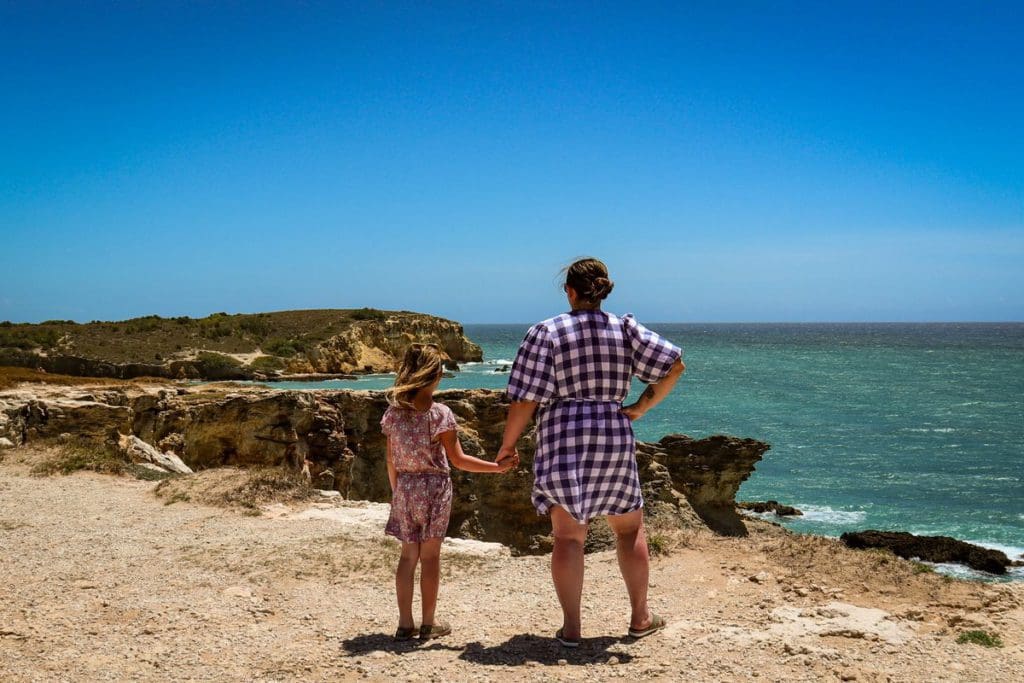 A mom and daughter hold hands as they look out over the cliffs and ocean while exploring Cabo Rojo National Wildlife Refuge in Puerto Rico.