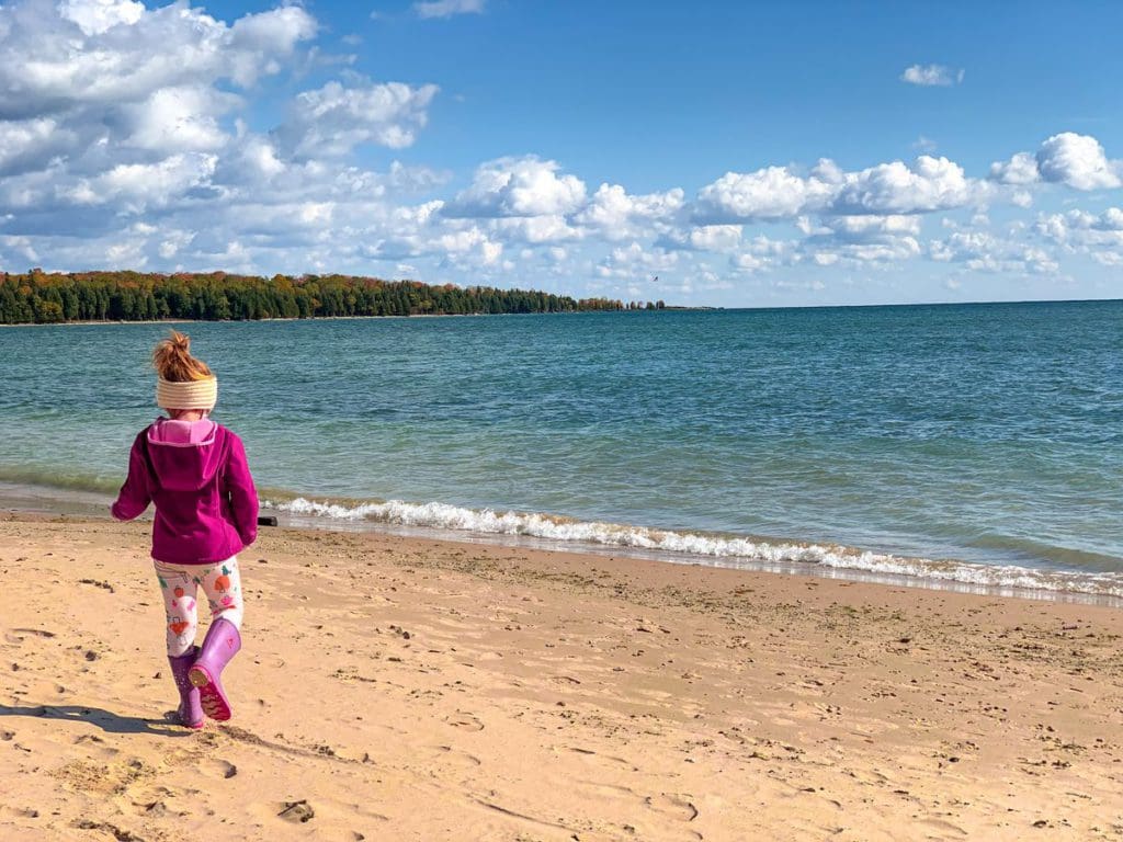 A young girl walks along a sandy beach with turquoise waters beyond her on Washington Island in Wisconsin.