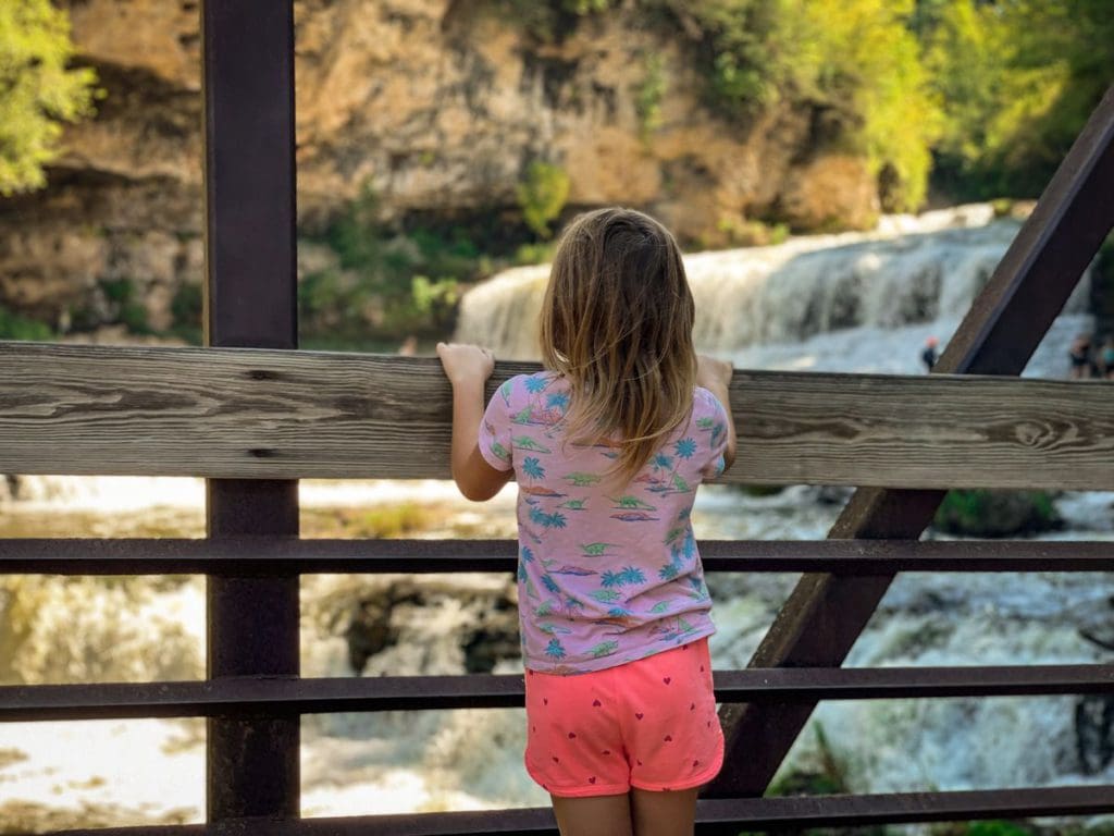 A young girl looks over a railing at the waterfall in Willow River State Park.