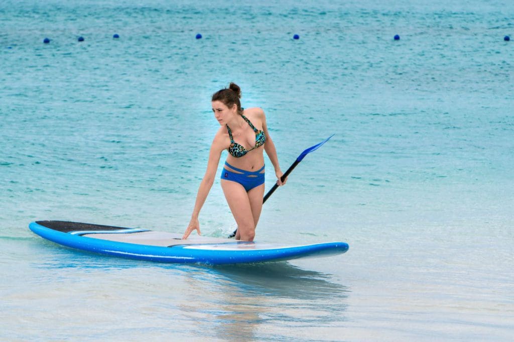 A woman walks along the shore, leading a stand-up paddleboard, along the beach in Barbados.