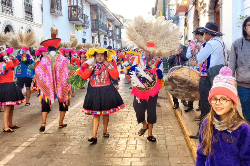 A young girl enjoys a vibrant parade of dancers on a street in Cusco, one of the best places to visit during Easter with your family.