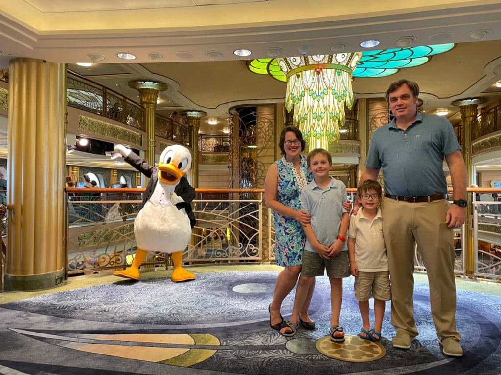 A family of four poses with Donald Duck, outfitted in a tux, while sailing with Disney.