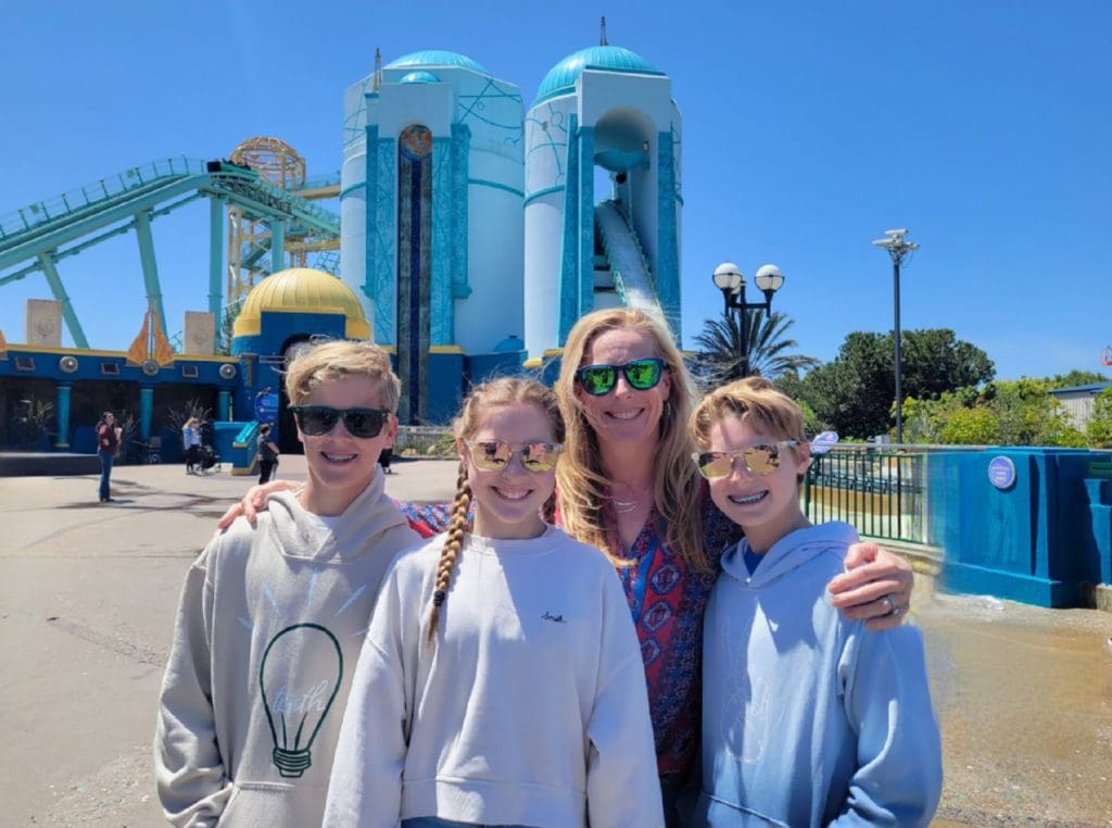A mom and her triplet teens stand together in front of a large ride at SeaWorld San Diego.