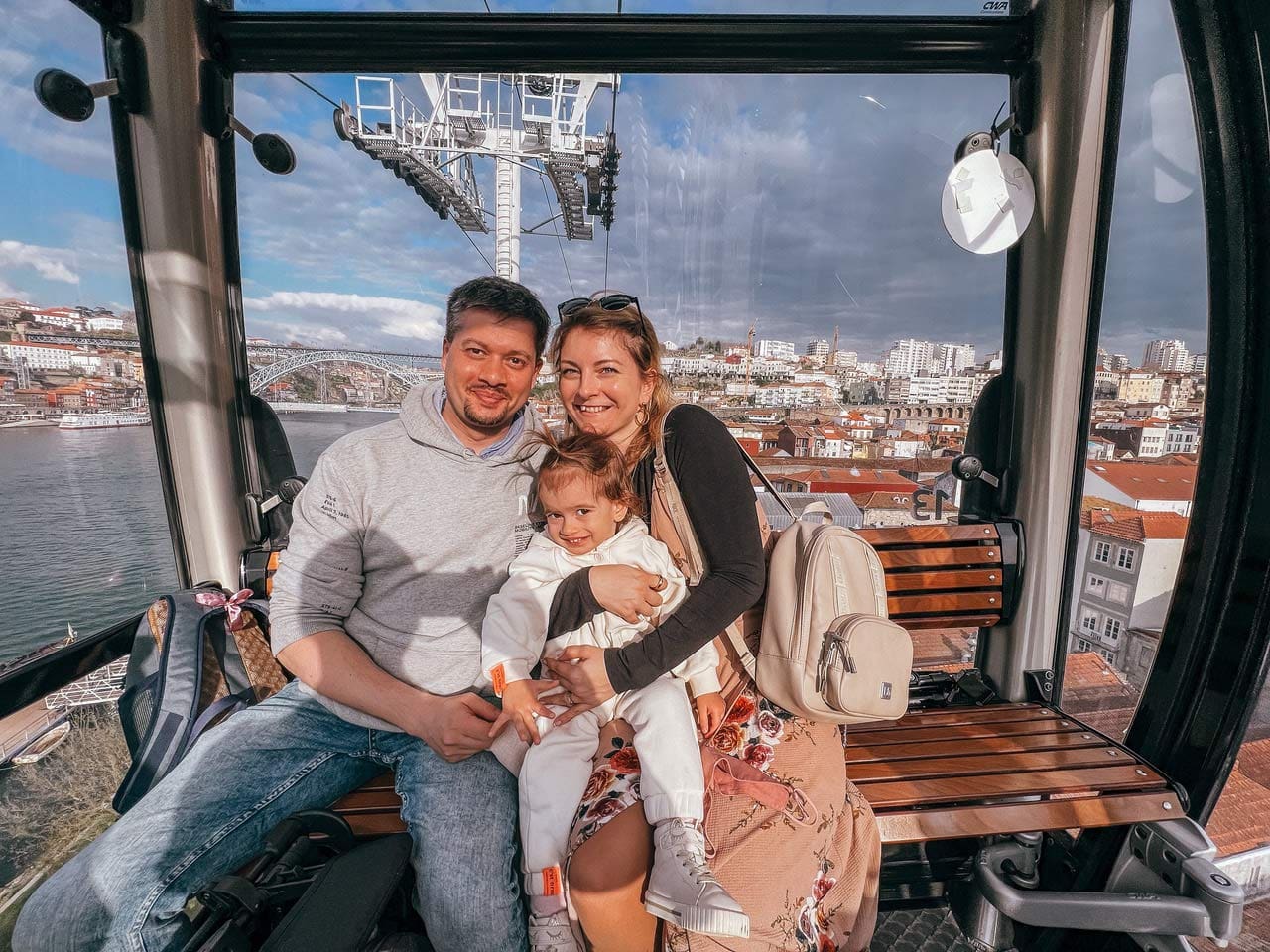 A family of three sits together and smiles in the Porto cable car.