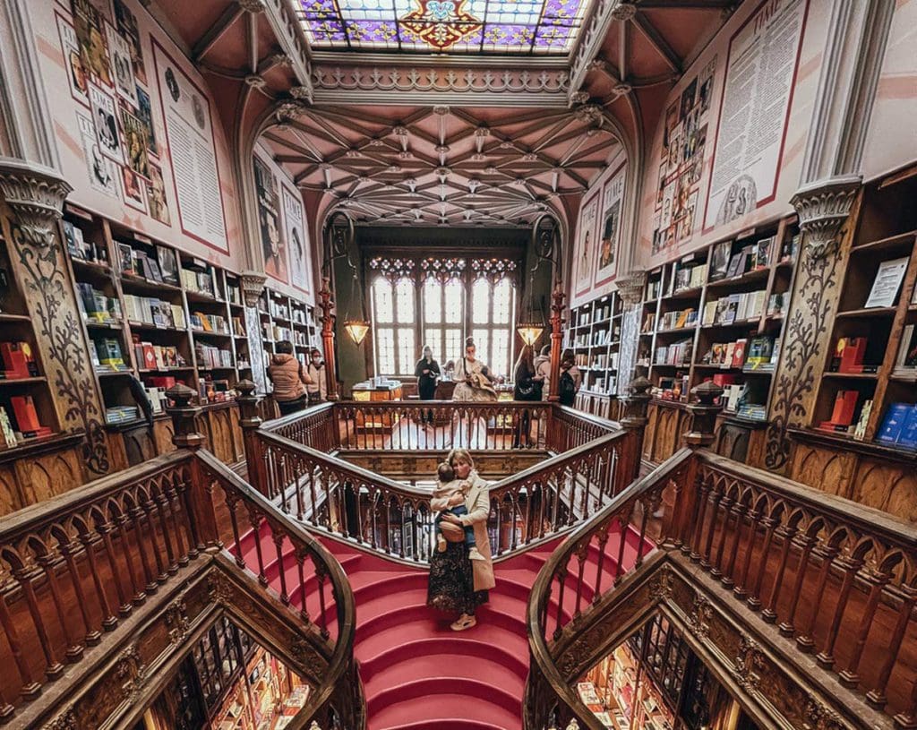 A mom and her young toddler stand on the iconic staircase of Livraria Lello in Porto.