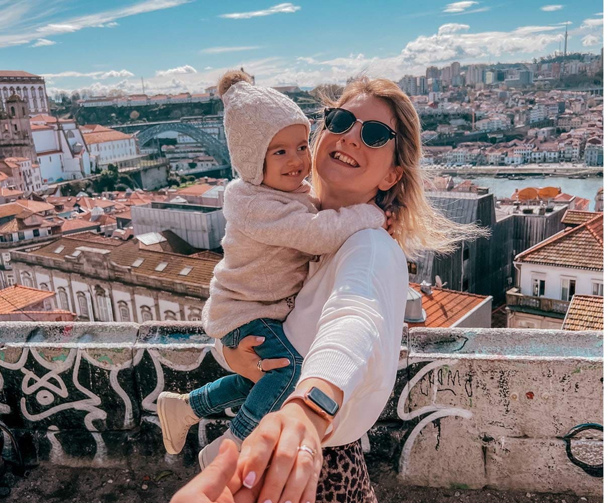 A mom holds her toddler, with a view of Porto in the distance, one of the top places in travel in 2023 with kids.