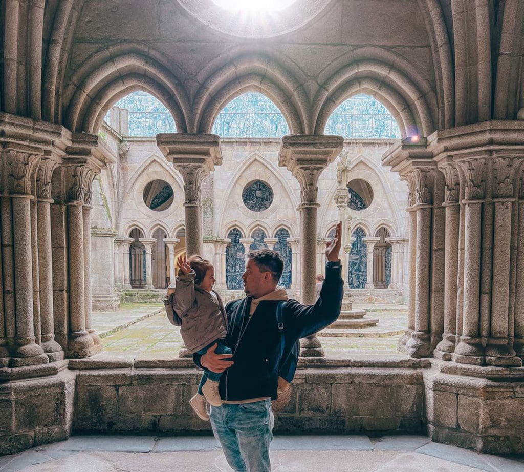 A dad holds his young daughter with large windows leading to a courtyard at Se Cathedral, a must stop on our 1-Week Porto itinerary with toddlers.