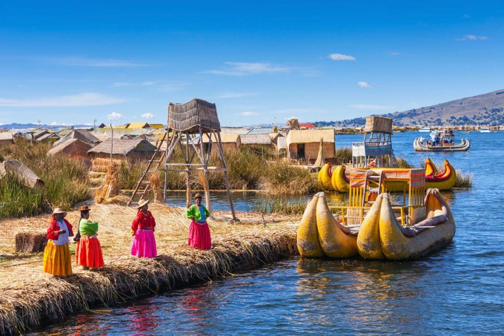 Several Peruvian woman stand on the edge of Lake Titicaca, with boats nearby.