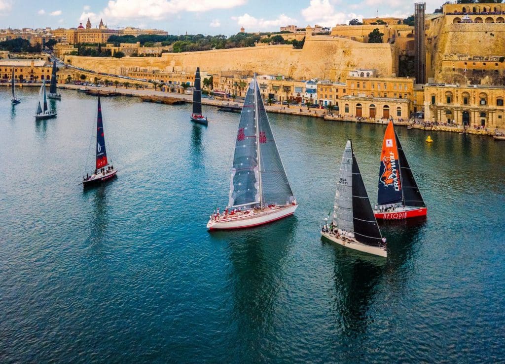 A shoreline of Malta, featuring several sail boats in the water.