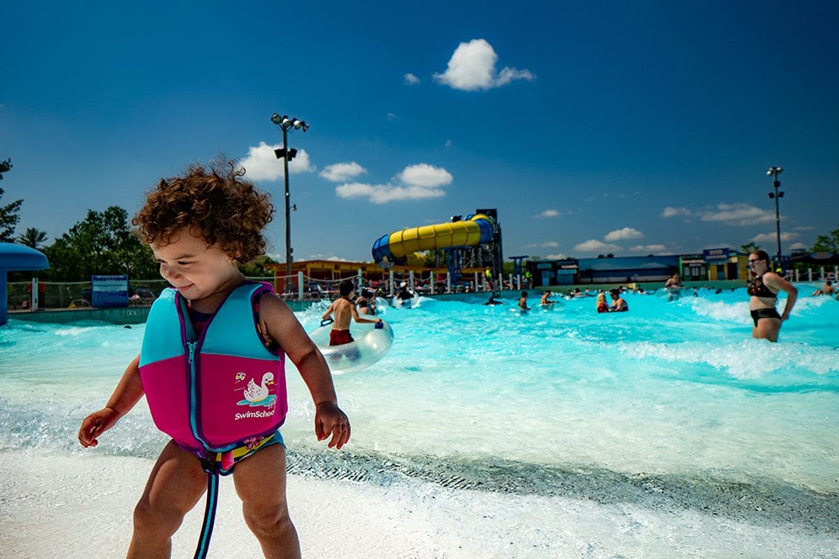 A young girl walks in front of the wave pool at Noah’s Ark Waterpark, with large water slides in the distance.