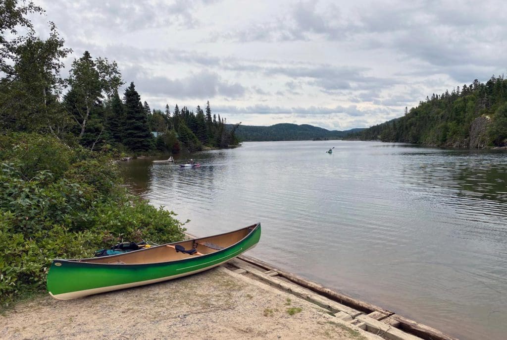 A canoe rests along a shore ready to head out onto the water, with trees flanking both sides of the water, in Pukaskwa National Park.