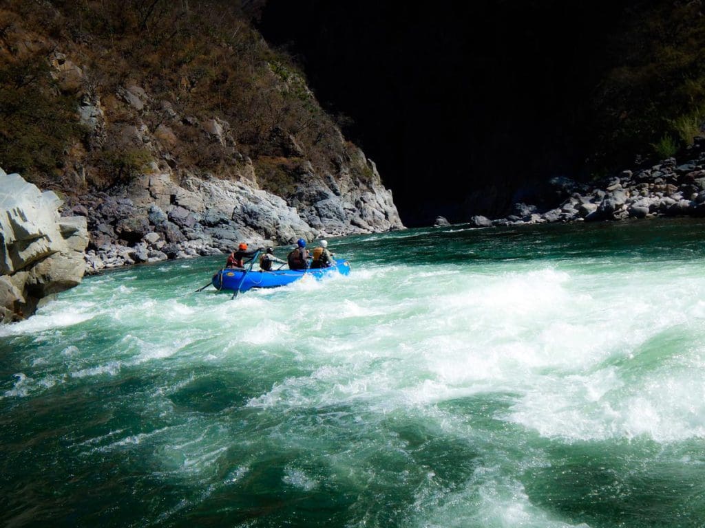 Several people, on a River Explorers tour, paddle along the low rapids in a raft in Peru, a must do on our Peru family vacation itinerary.
