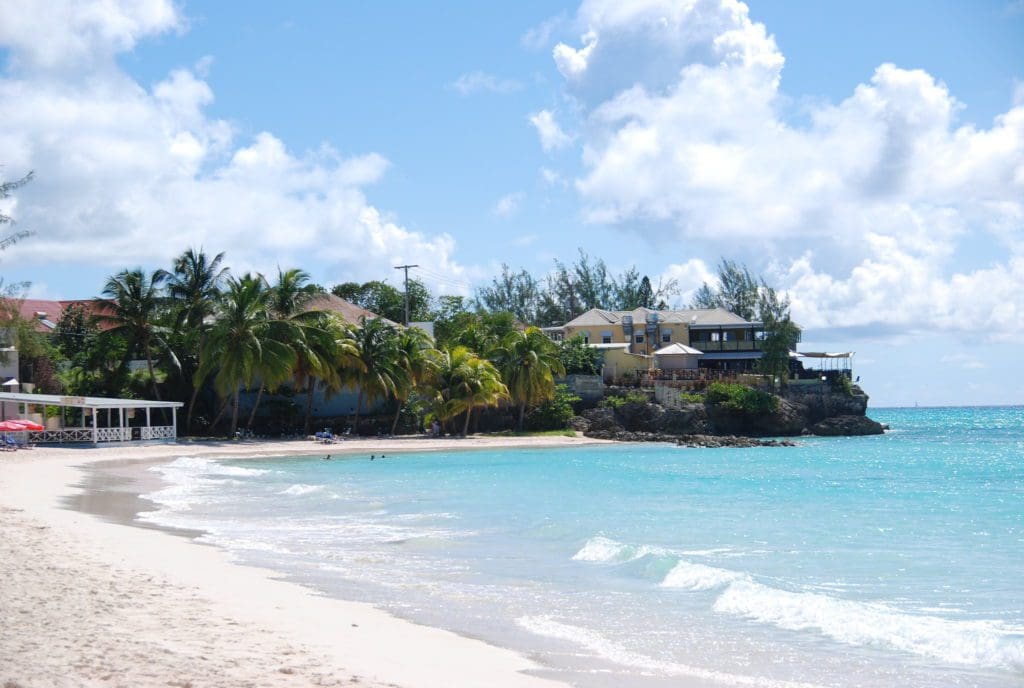 Rockley Beach in Barbados, featuring white sands and crystal blue waters, with a tree line shore on the far end.